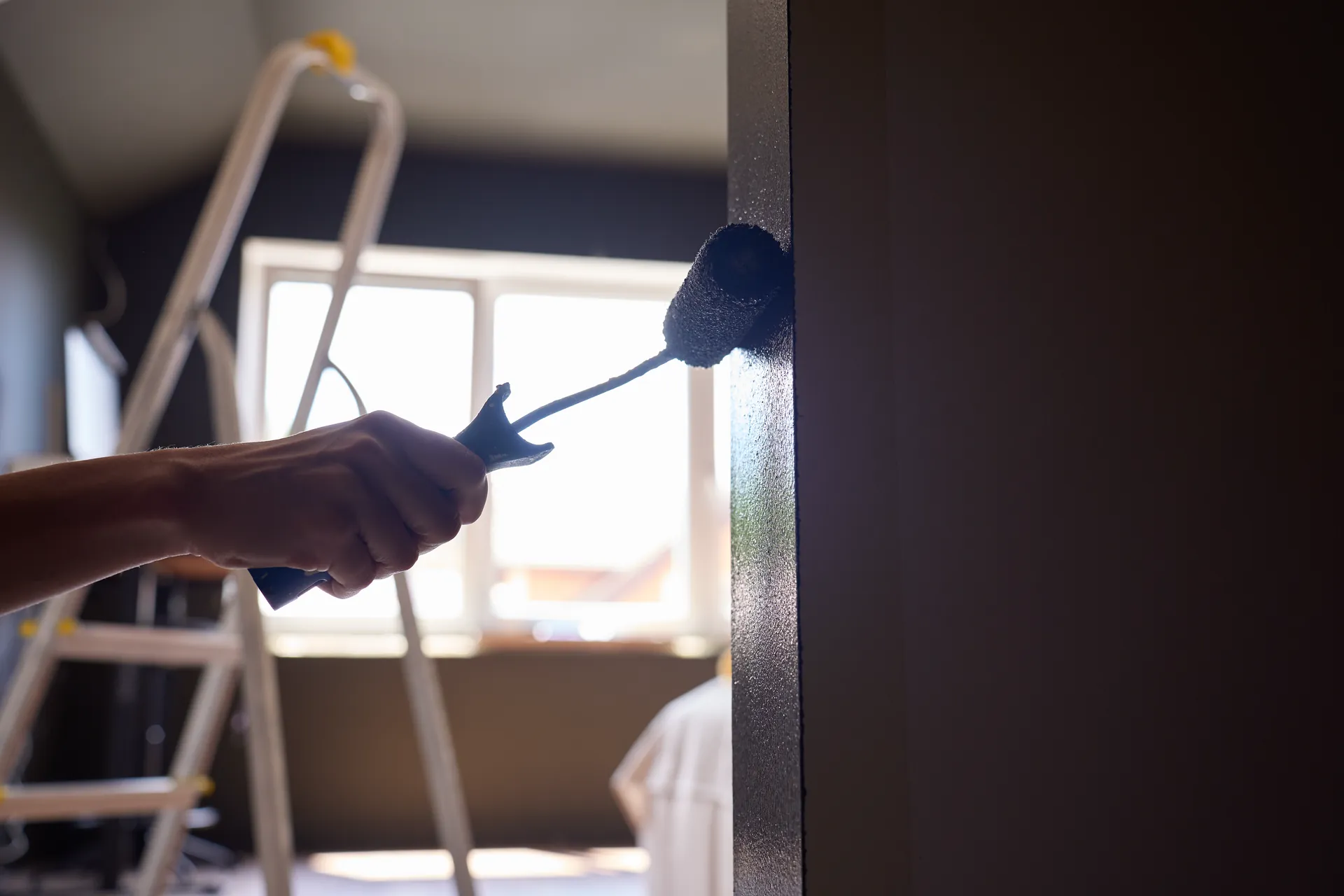 Farbrolle zieht eine saubere Kante entlang der Wand, Gegenlicht vom Fenster