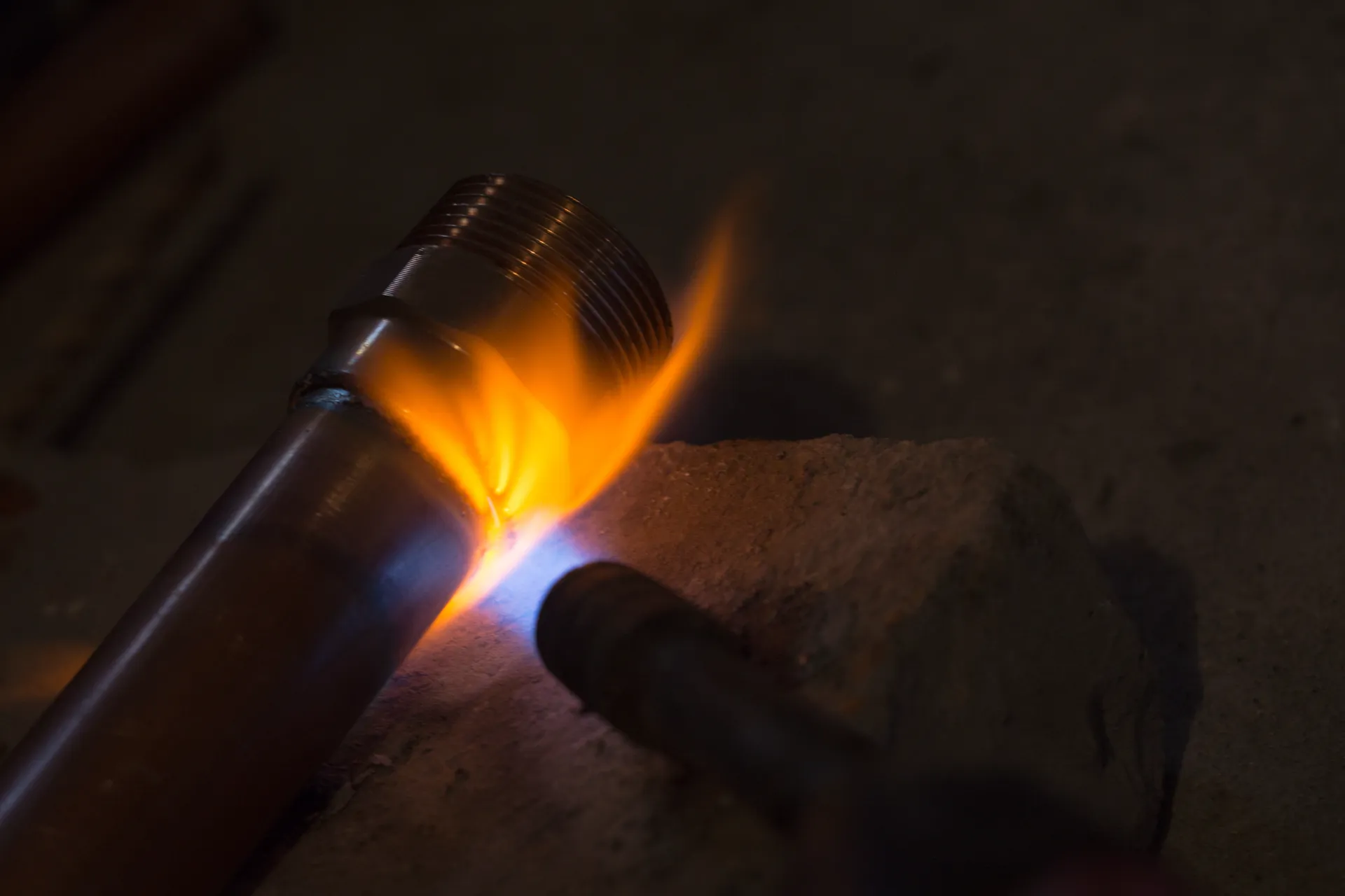 Handwerker lötet mit blauer Flamme ein Kupferrohr auf dem Estrich